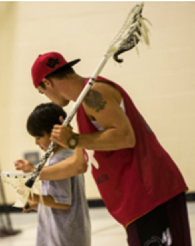 Picture of Chet Koneczny helping a young lacrosse player.